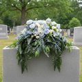 Mixed Blues Floral Memorial Saddle on a grey granite headstone monument, with dusty blue roses, hydrangeas, cream blooms, and cascading ferns