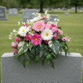 Handcrafted pink and white floral memorial saddle arrangement with gerbera daisies, sweet peas, white daisies, and lush cascading greenery, displayed on a grey granite headstone in a peaceful cemetery setting — custom made by GG's Handmade Creations in Scotch Village, Nova Scotia
